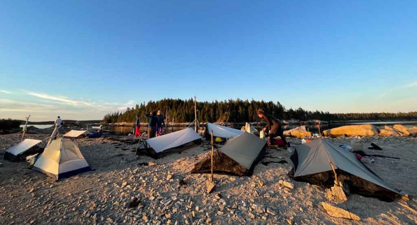 A campsite with a tarp shelters rests on a sandy beach